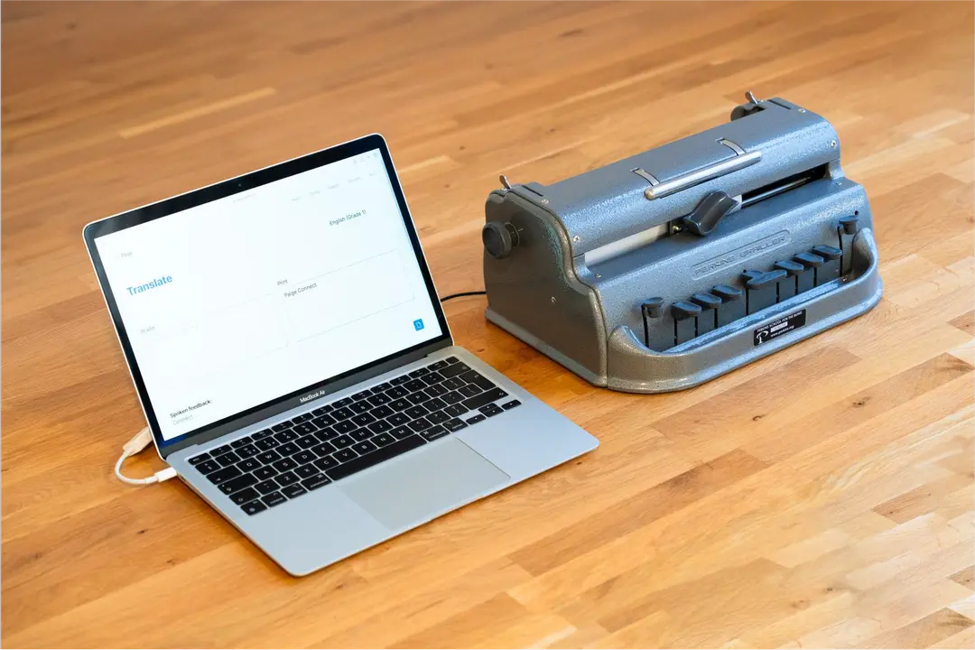 Braille writer with Paige Connect connected to a laptop. The laptop screen shows translated braille.